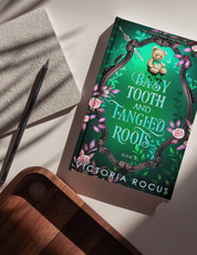 Book titled 'Baby Tooth and Tangled Roots' by Victoria Rocus on a surface with a pen and notebook.