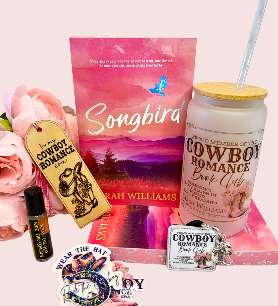 Collection of 'Songbird' book box with tumbler, and related merchandise on a pink surface.
