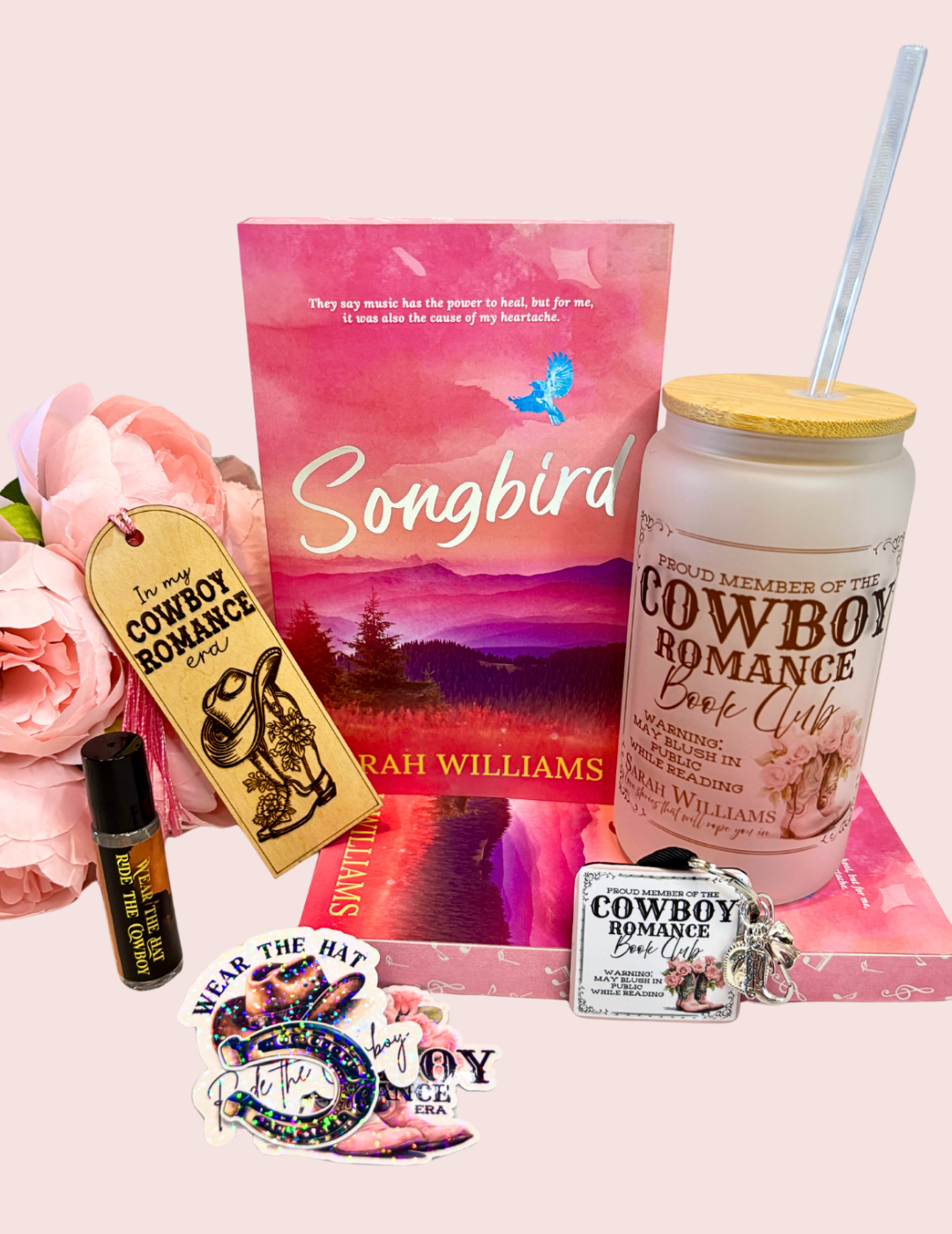 Collection of 'Songbird' book box with tumbler, and related merchandise on a pink surface.