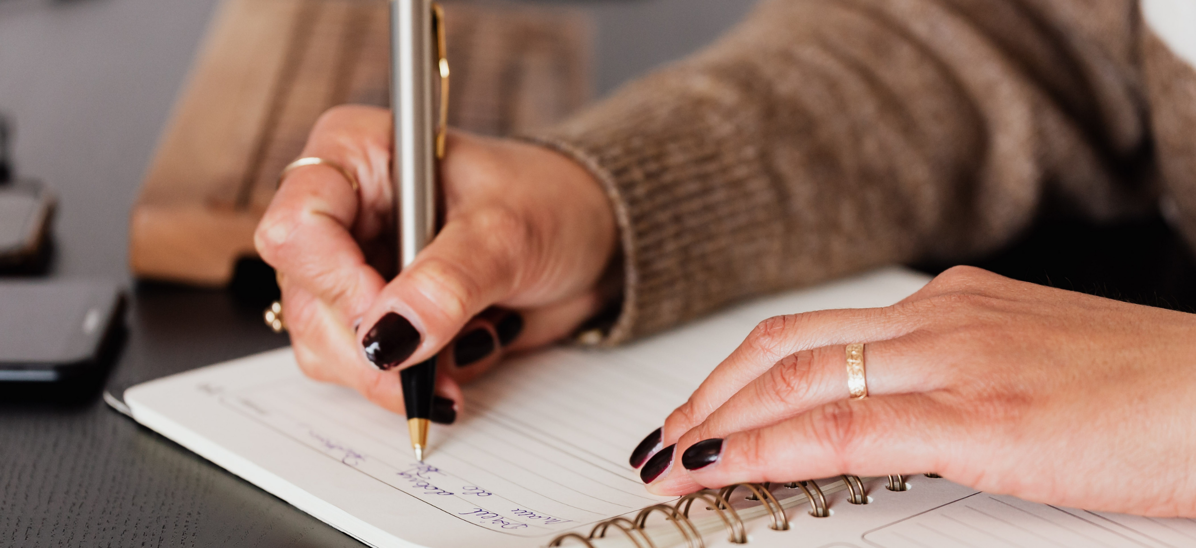 Person writing in a notebook with a pen on a desk.