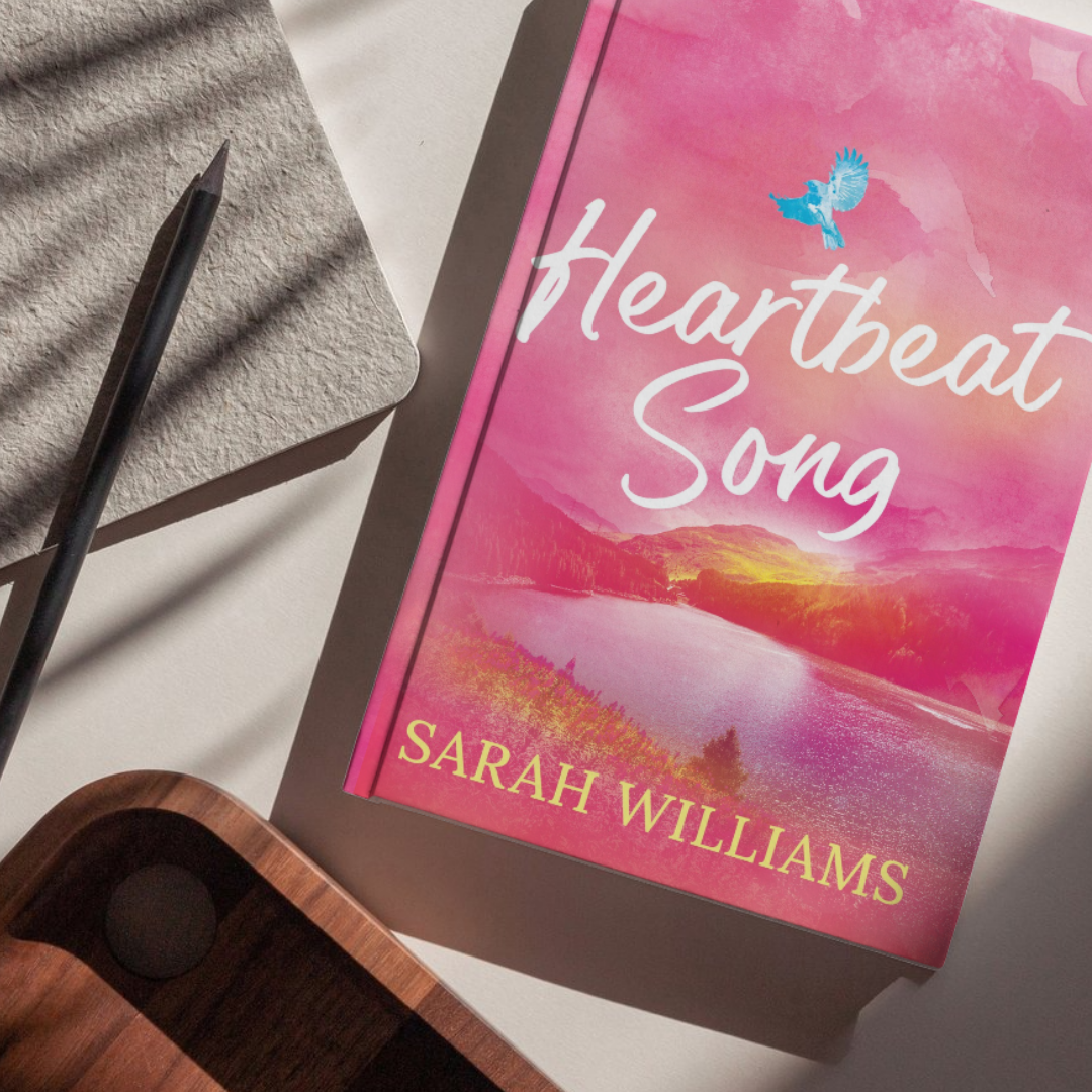 Book titled 'Heartbeat Song' by Sarah Williams on a surface with a pen and phone.