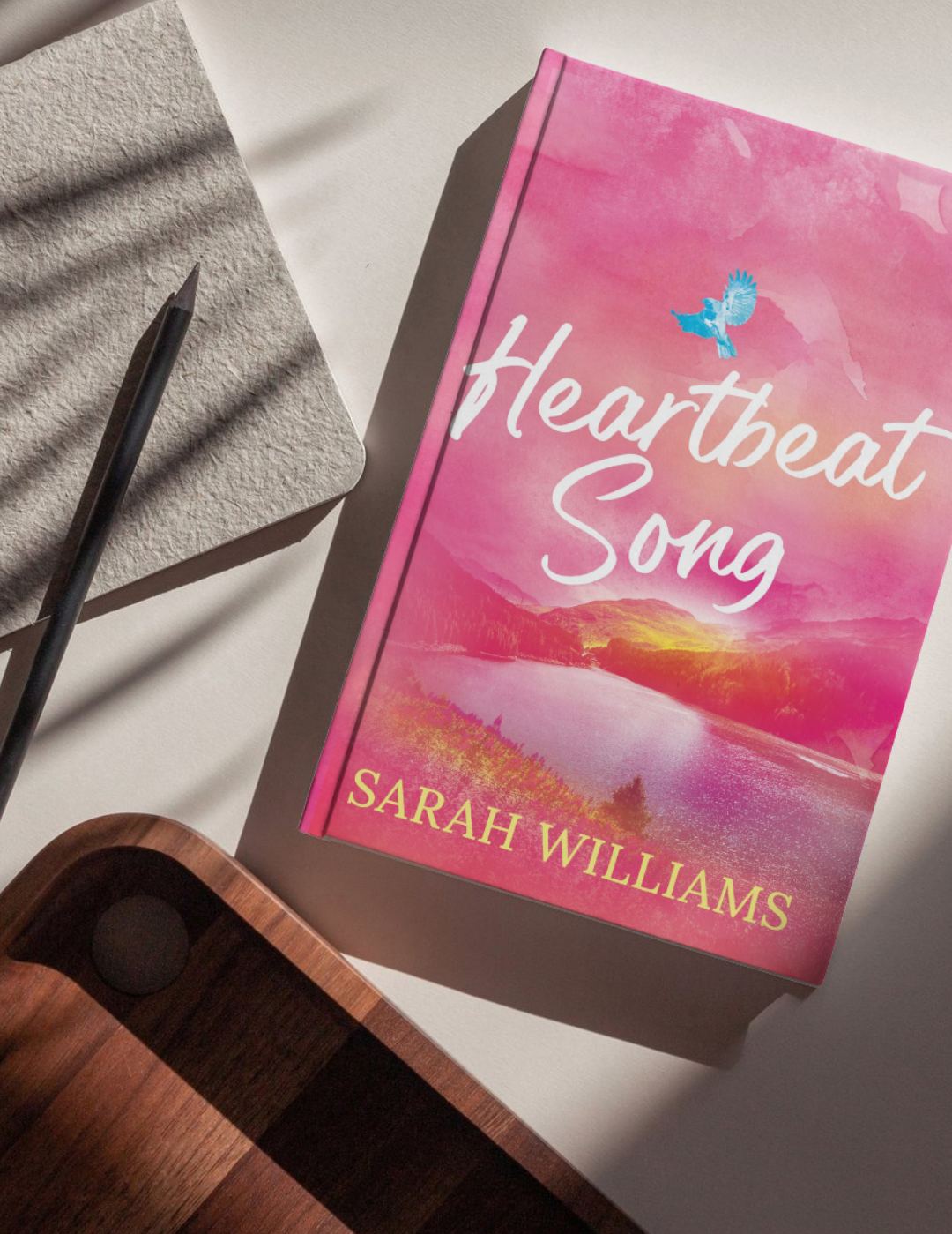Book titled 'Heartbeat Song' by Sarah Williams on a surface with a pen and phone.
