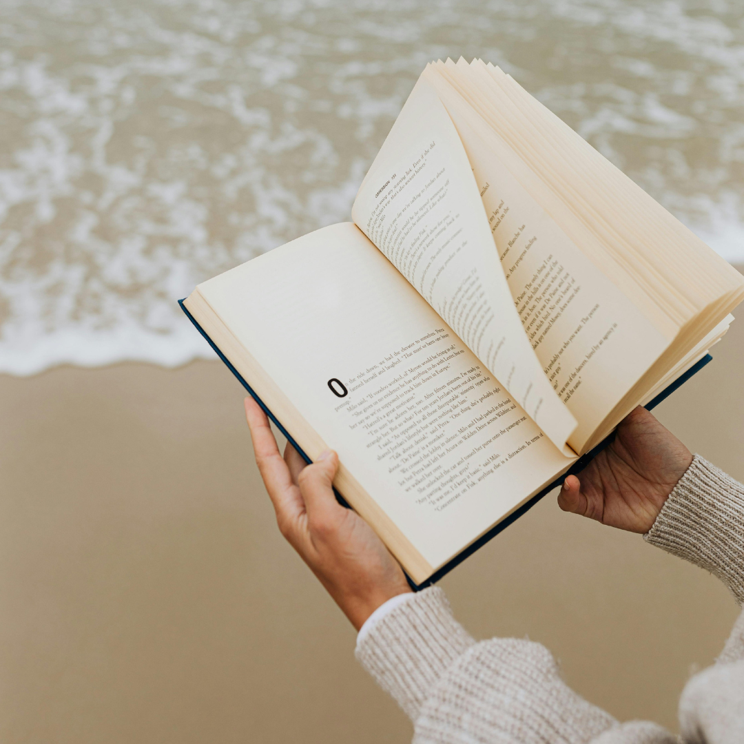 Open book held by a person on a beach with waves in the background