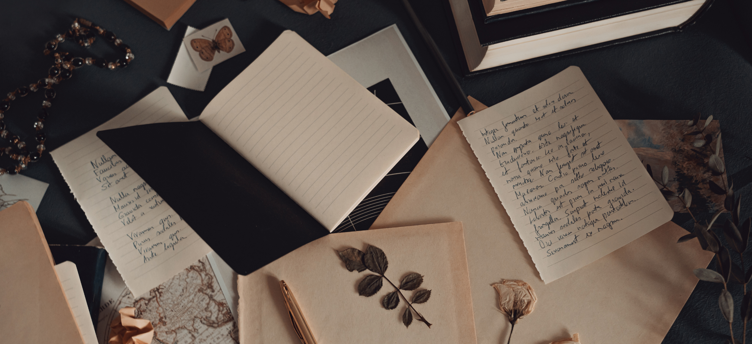 Open notebook with handwritten text surrounded by other books and papers on a dark surface.