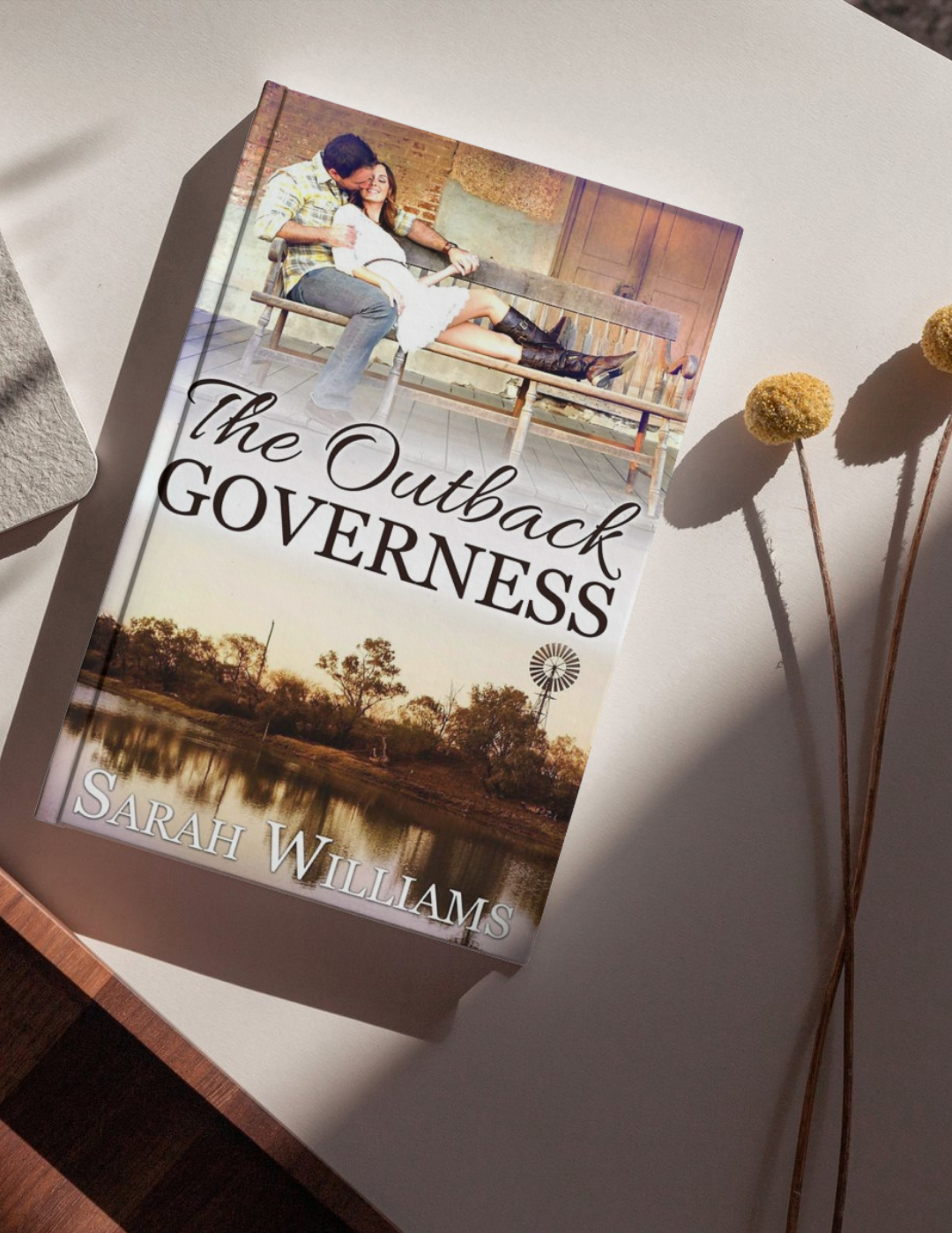 Book titled 'The Outback Governess' by Sarah Williams on a surface with a scenic cover.