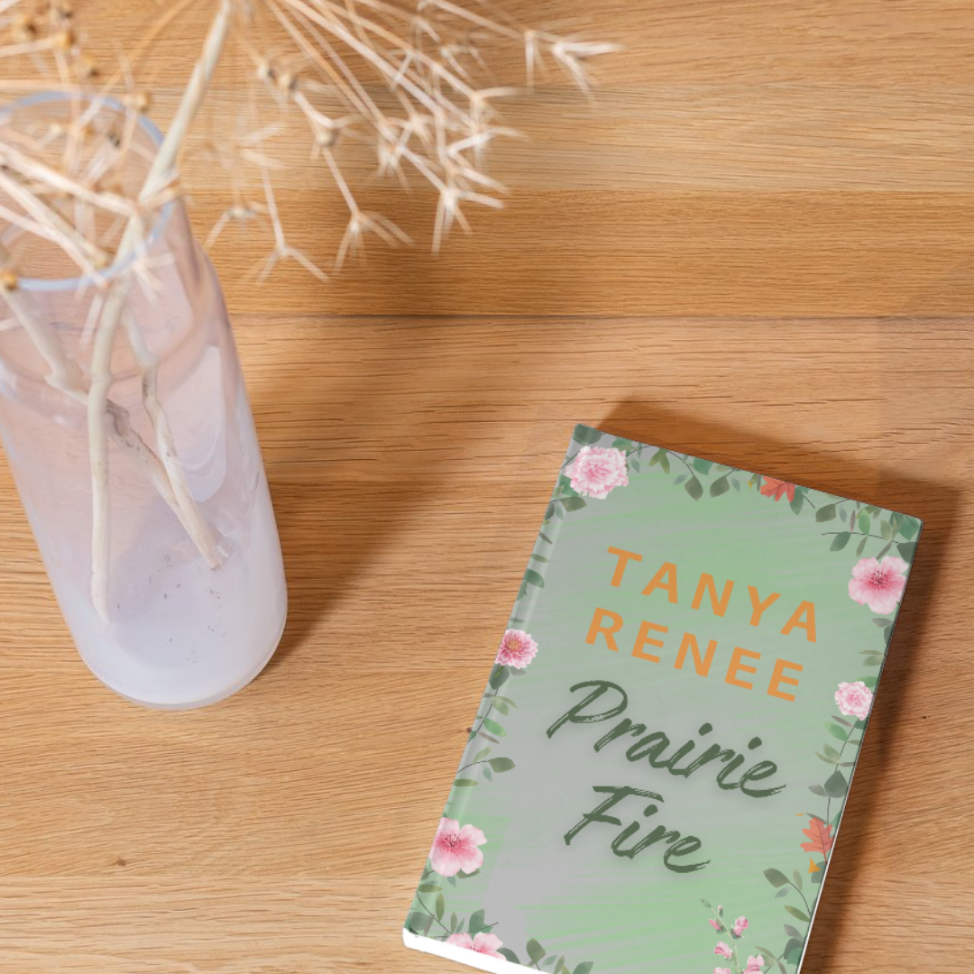 Book titled 'Prairie Fire' by Tanya Renee on a wooden surface with a vase of dried flowers.