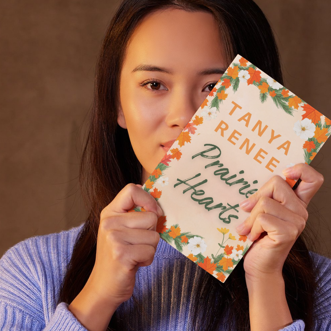 Woman holding a book titled 'Prairie Hearts' by Tanya Renee against a brown background