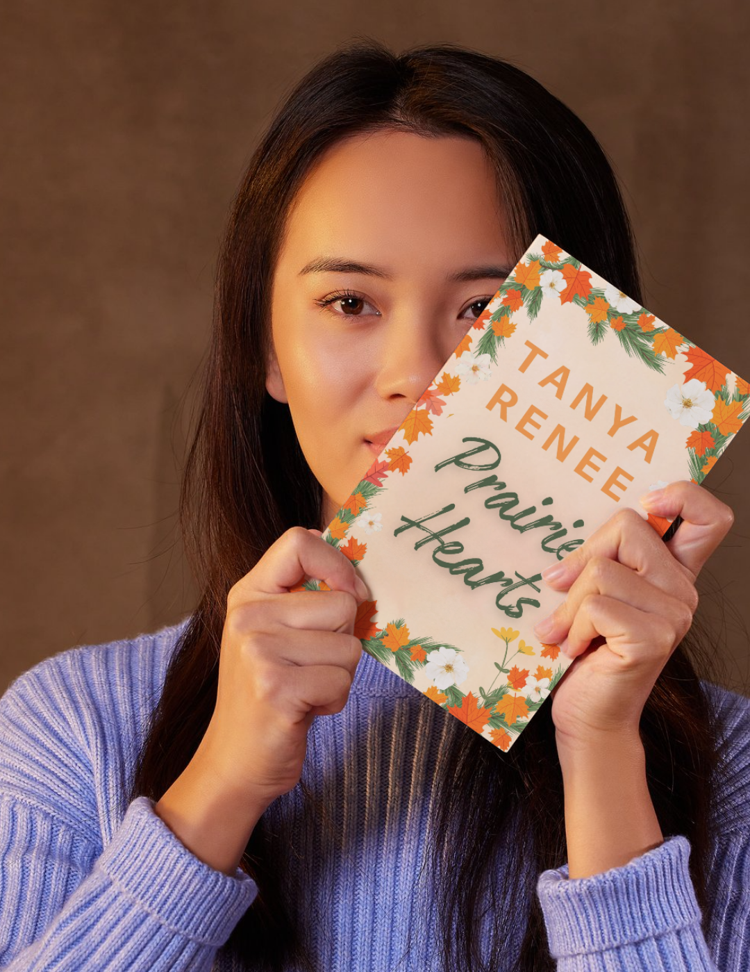 Woman holding a book titled 'Prairie Hearts' by Tanya Renee against a brown background