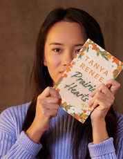 Woman holding a book titled 'Prairie Hearts' by Tanya Renee against a brown background