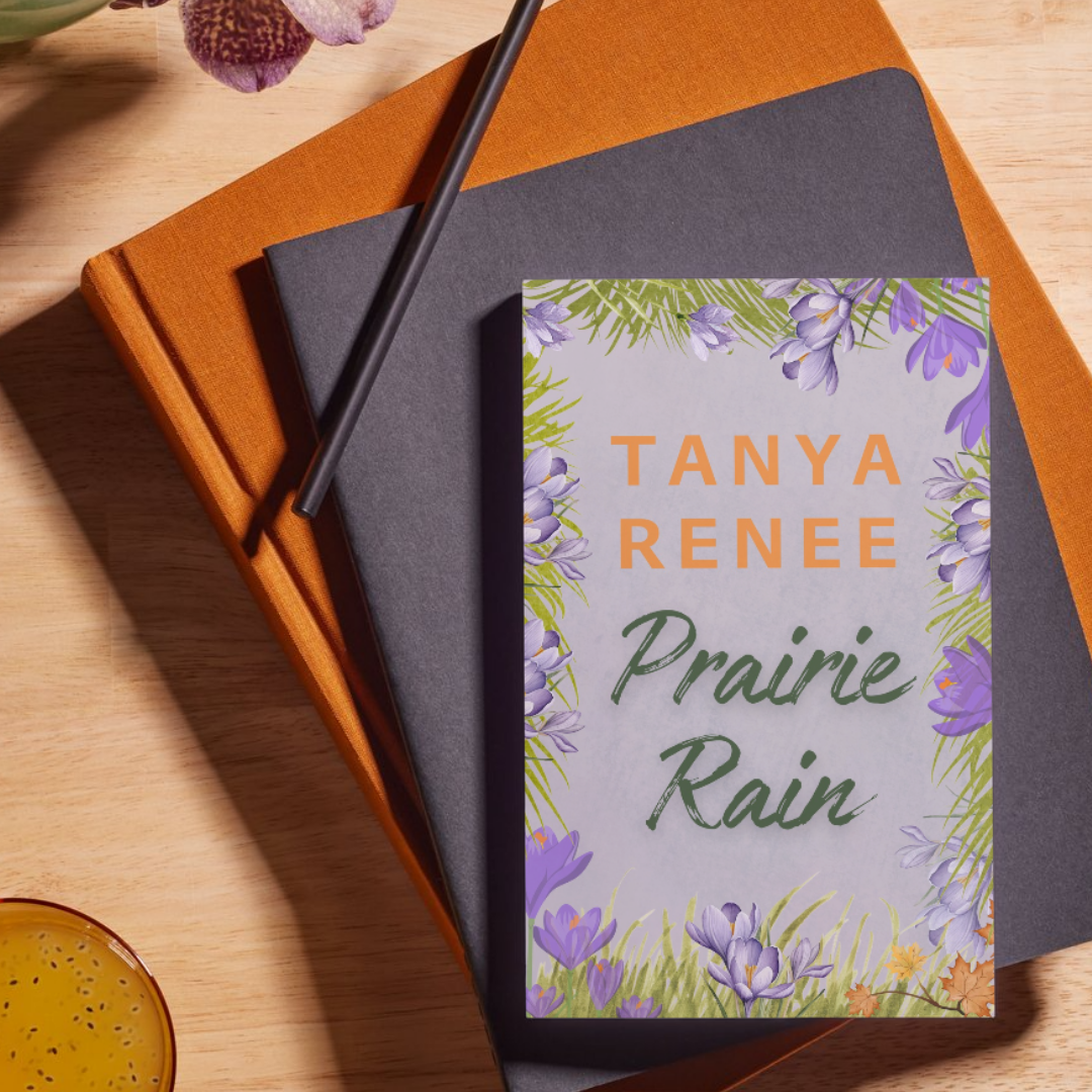 Book titled 'Prairie Rain' by Tanya Renee on a wooden surface with a pen and notebook.