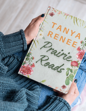 Book titled 'Prairie Roads' by Tanya Renee held by a person wearing a blue sweater.