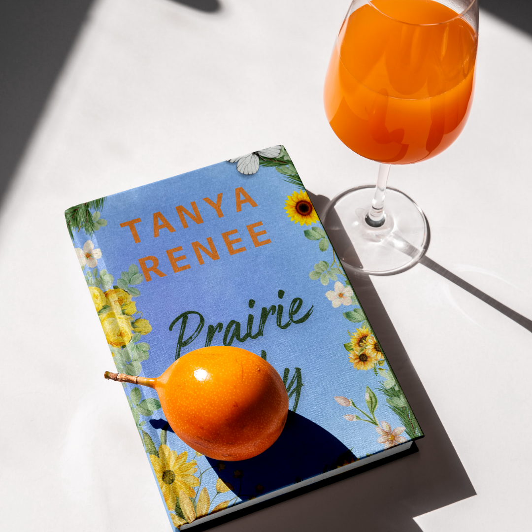 Book titled 'Prairie Sky' by Tanya Renee with a glass of orange juice on a white surface.