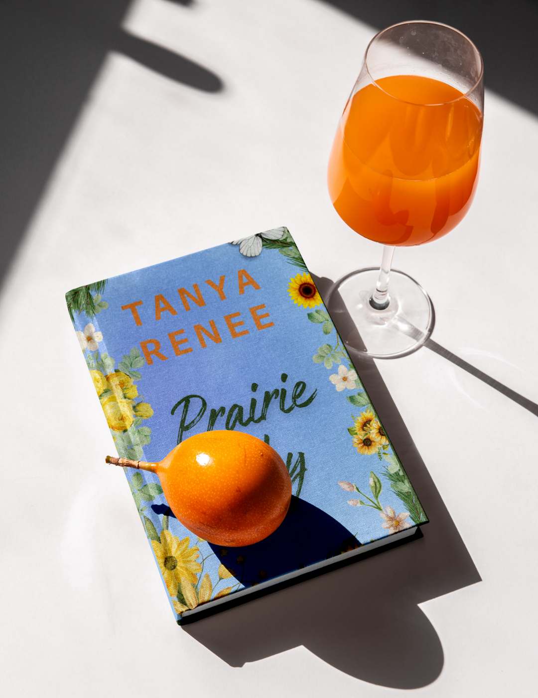 Book titled 'Prairie Sky' by Tanya Renee with a glass of orange juice on a white surface.
