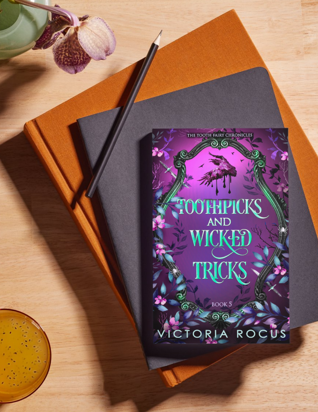 Book titled 'Toothpicks and Wicked Tricks' by Victoria Rocus on a wooden surface with a pencil and cup.