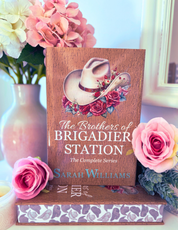 Book titled 'The Brothers of Brigadier Station' by Sarah Williams with floral design on a decorative stand, surrounded by flowers.