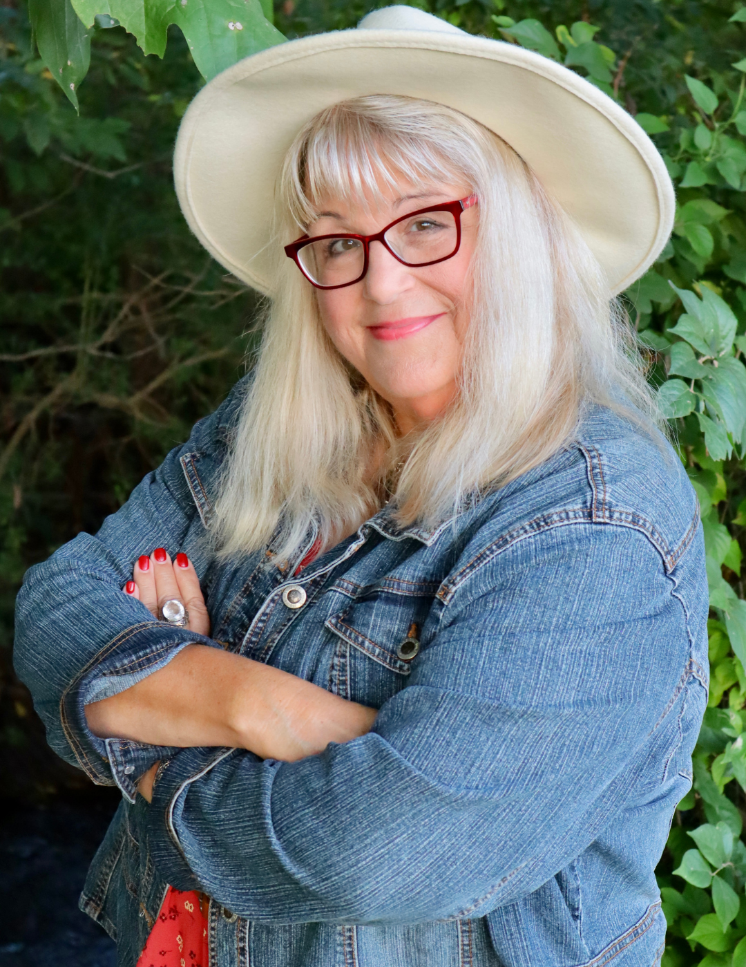 Author Victoria Rocus wearing a wide-brimmed hat and denim jacket with a green leafy background