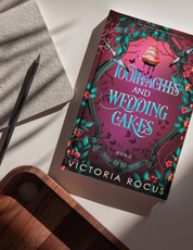 Book titled 'Toothaches and Wedding Cakes' by Victoria Rogus held by a person with water in the background